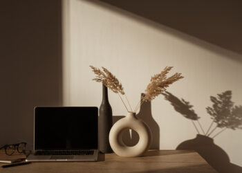 Laptop computer with blank screen on table with pampas grass bouquet in sunlight shadows on the wall. Aesthetic influencer boho styled office workspace interior design template with mockup copy space