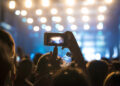 Woman in the crowd taking picture of stage at music festival.